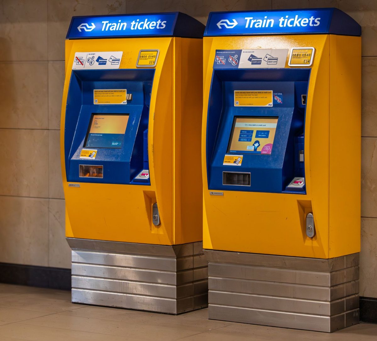 Two vibrant yellow and blue train ticket machines in an indoor station setting.