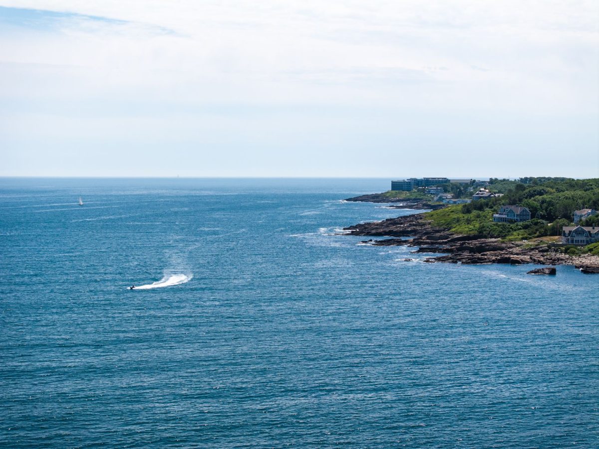 Captivating coastal view of Ogunquit, Maine, showcasing blue ocean waters, rocky shoreline, and a distant jet ski.