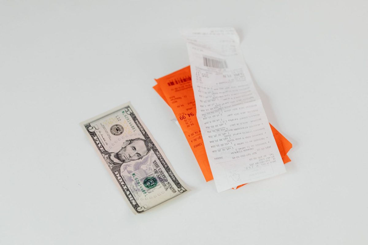 Close up of a five dollar bill next to shopping receipts on a white background, ideal for finance and retail themes.