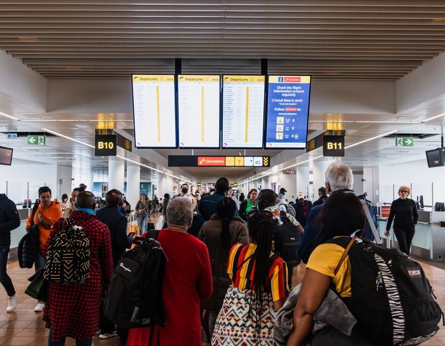 Travelers lining up in a busy airport terminal with baggage under flight information screens.