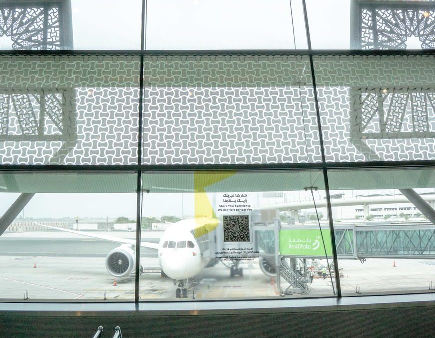 Interior view of airport terminal with aircraft on tarmac beyond glass windows.