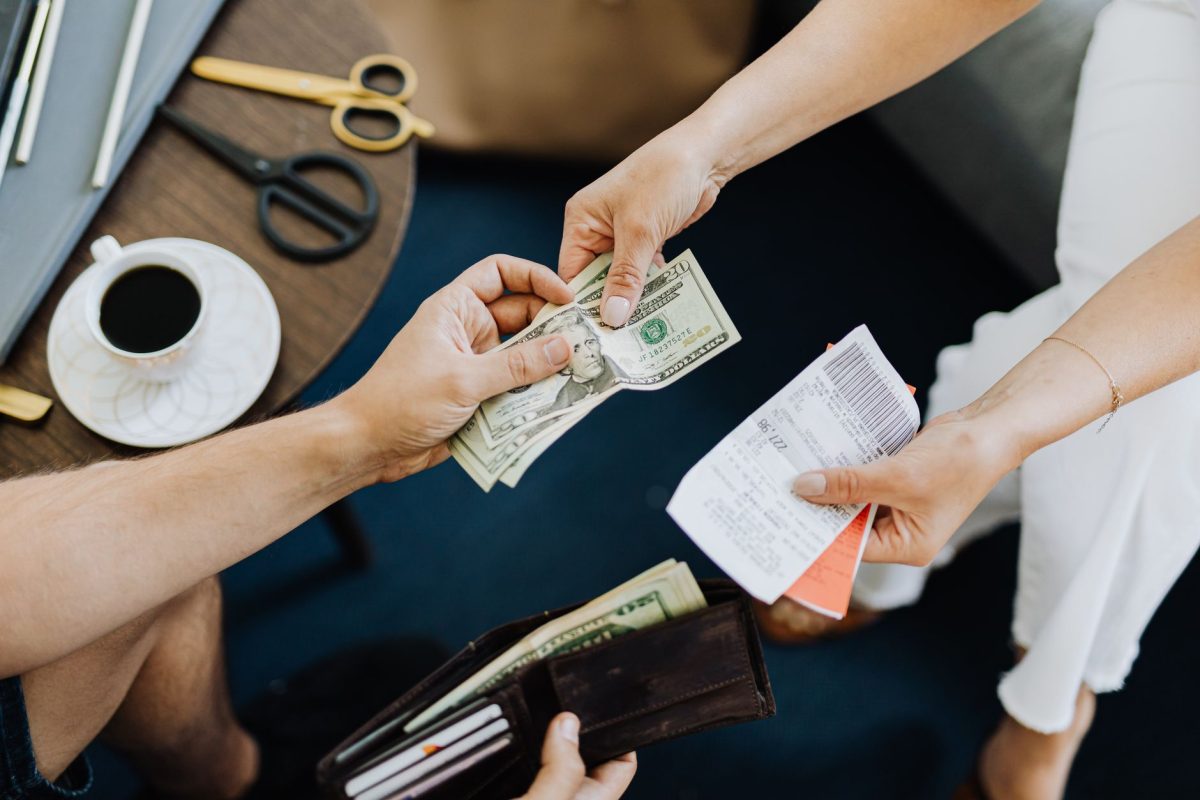 Close up of a transaction with US dollar bills and receipts being exchanged over a table with coffee and scissors.