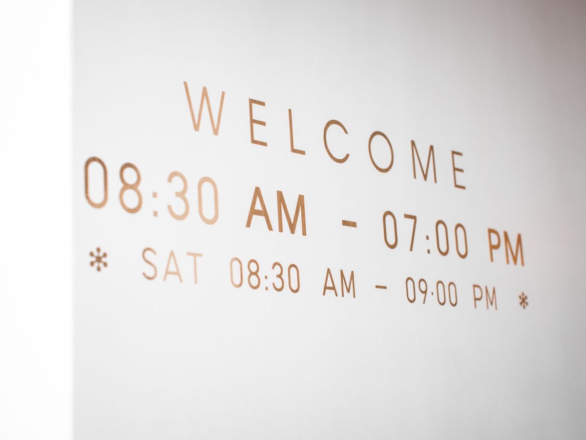 Close up of a minimalist welcome sign displaying business hours in stylish typography.