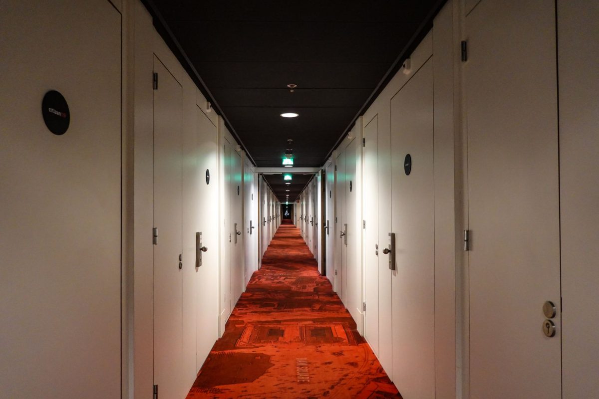 Long, symmetrical hotel hallway with red carpet and closed white doors under warm lighting.