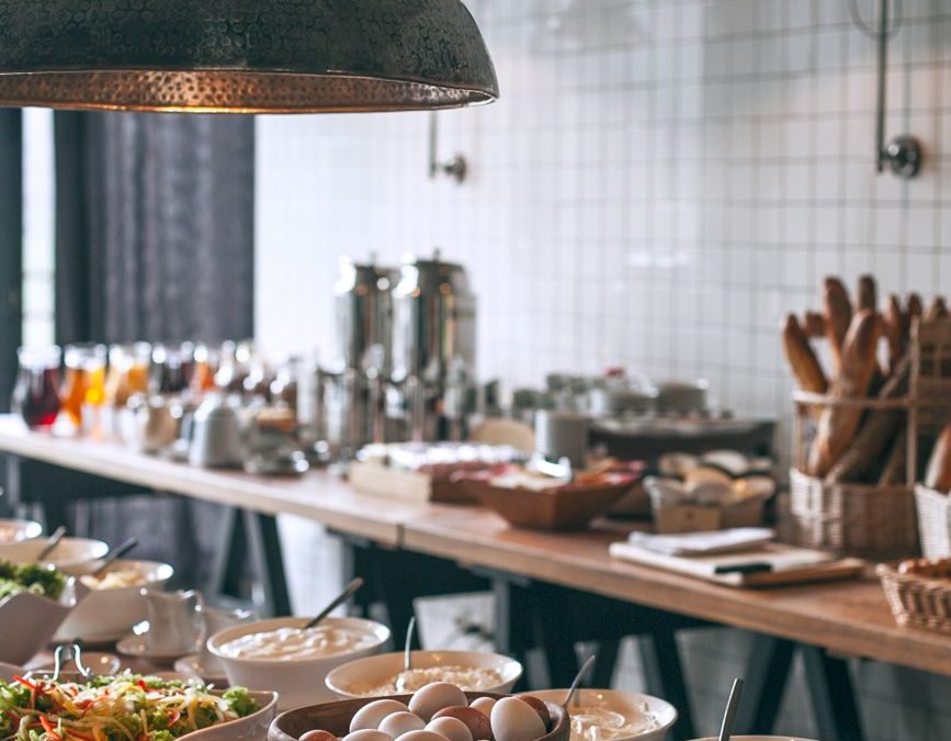 Bowls of tasty food served on banquet tables in light canteen with lamps and kitchenware and with other breakfast ingredients