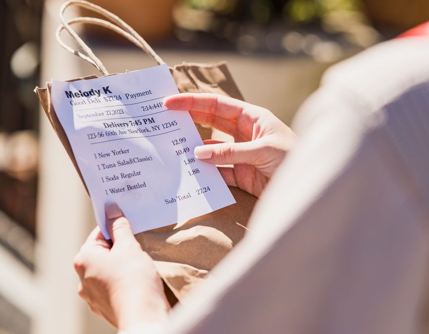 Close up of someone reading an order receipt attached to a delivery paper bag. Outdoor setting.