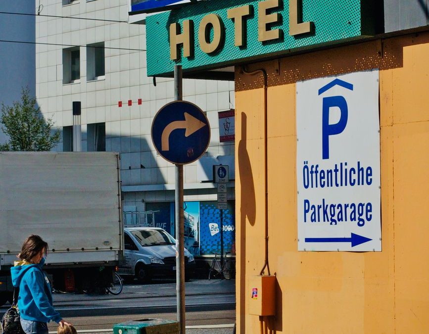Urban street scene featuring a hotel sign, public parking, and pedestrians.