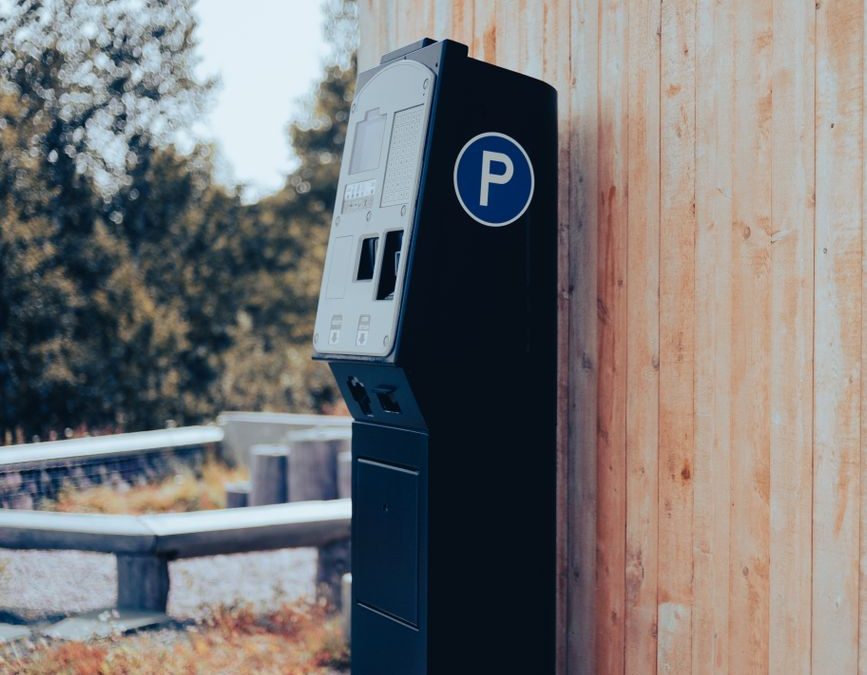 Photo of an outdoor parking ticket machine beside a wooden wall with natural surroundings.