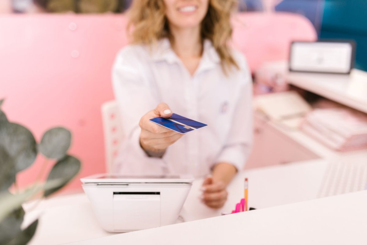 Blurred hands offering a credit card to a cashier at a modern retail counter.