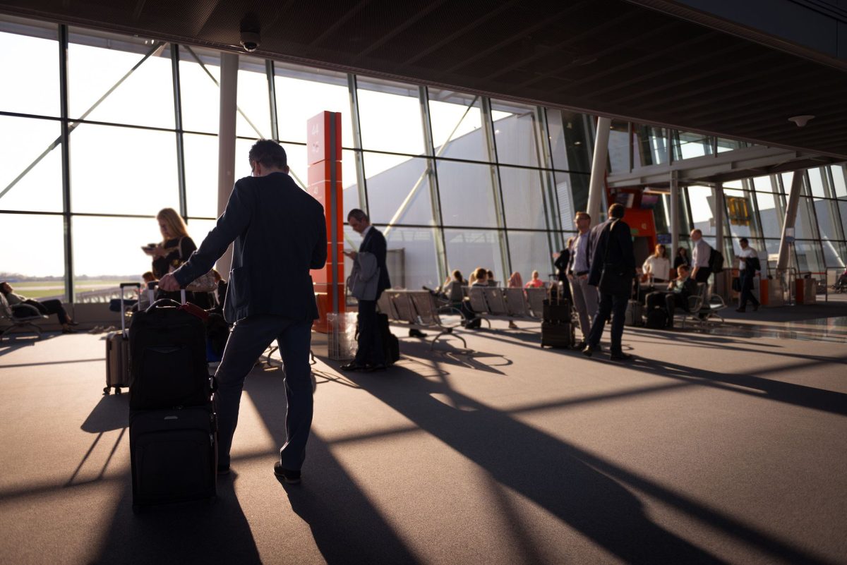 Travelers in a bustling airport terminal with carry on luggage waiting for departure.