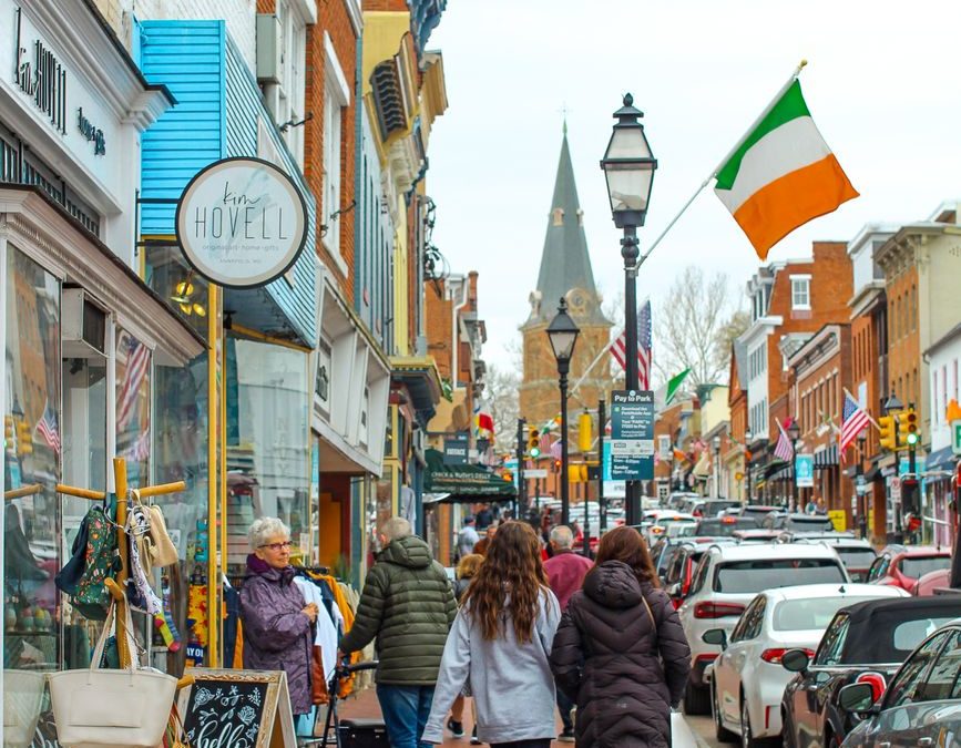 Bustling street scene in downtown Annapolis with people shopping and walking under flags.