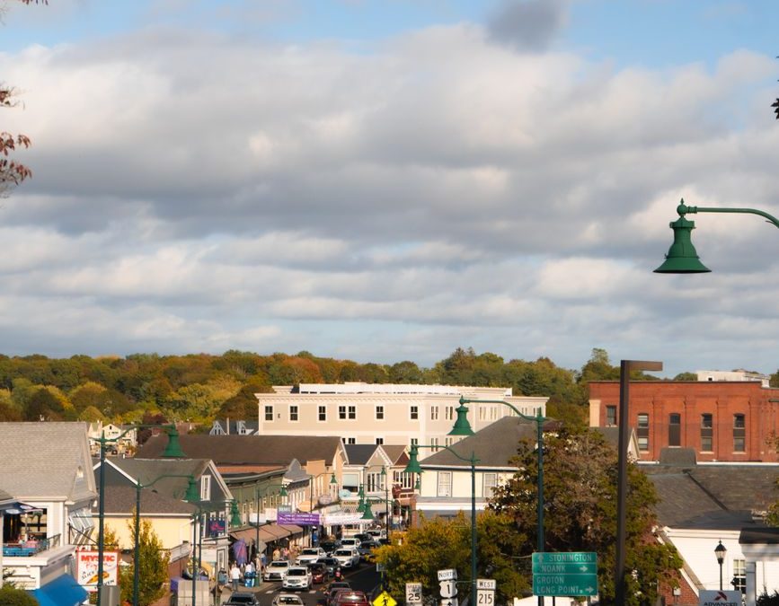 A bustling small town street with autumn foliage and traffic under a cloudy sky.