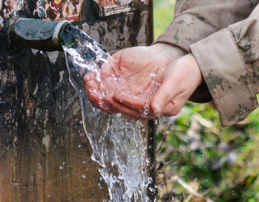Hands catching flowing water from an outdoor fountain, evoking natural refreshment.