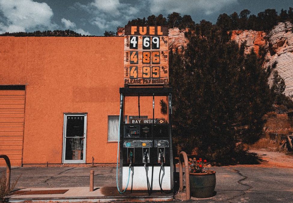 Old gas station with vintage pump and price sign under a cloudy sky. Outdoors setting.