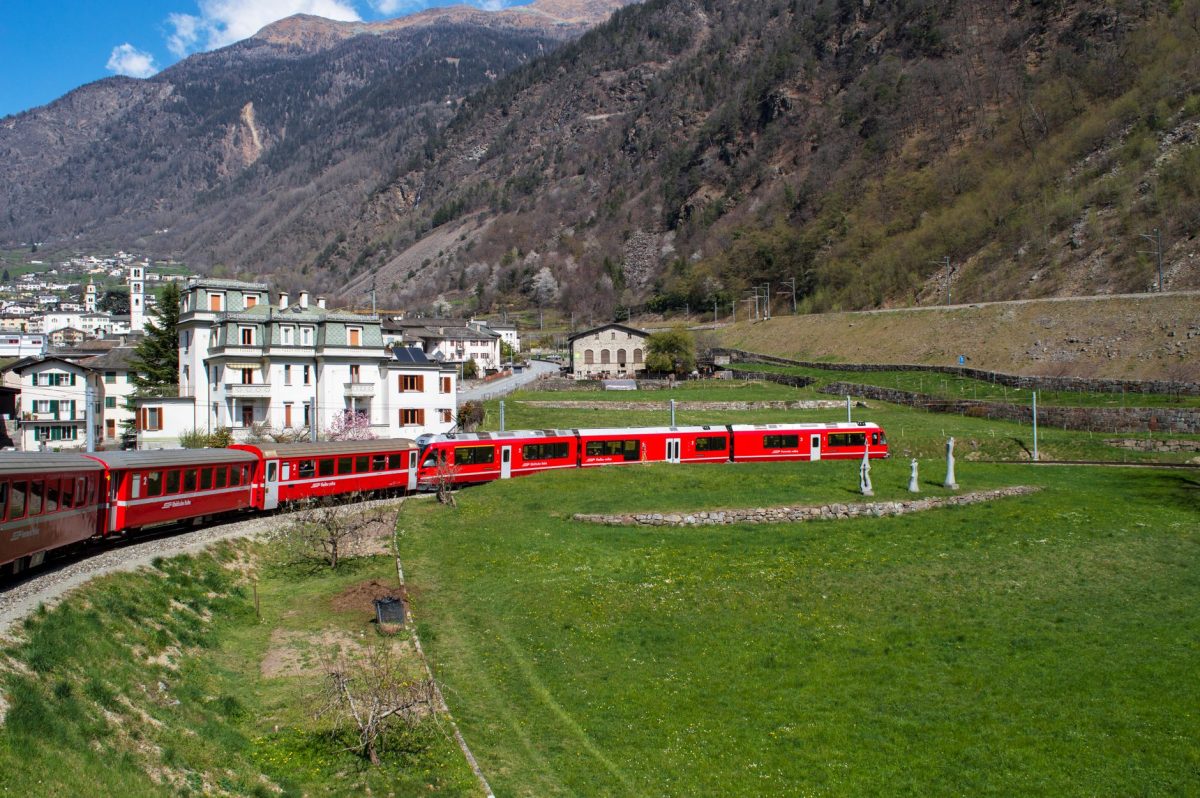 The iconic red Bernina Express train traverses a scenic valley in the Swiss Alps.