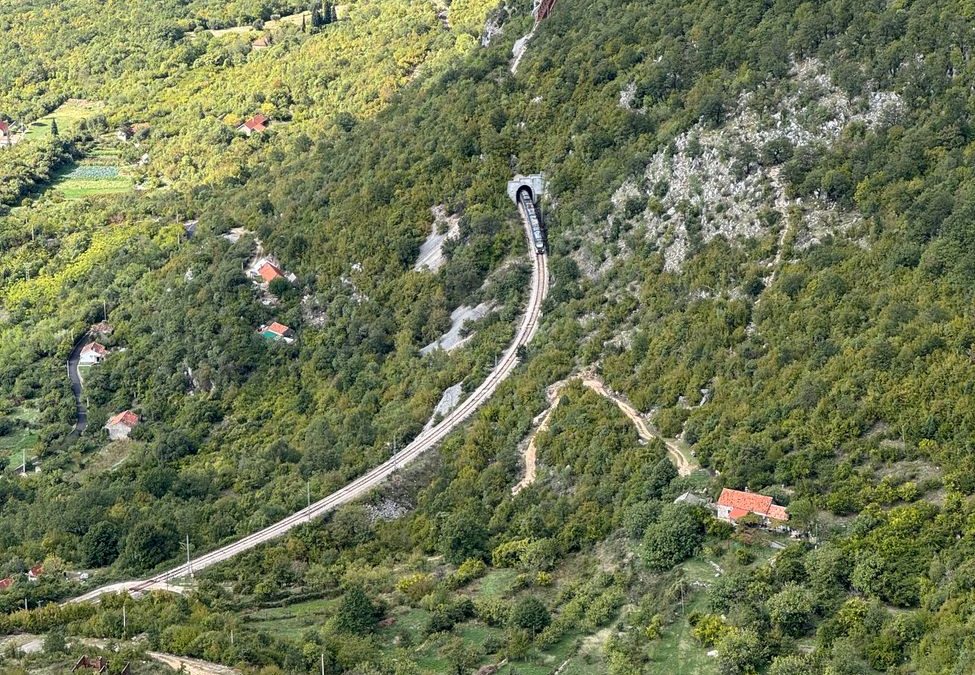 A picturesque railway tunnel cutting through lush green hills in Montenegro, capturing nature&amp;#39;s blend with infrastructure.