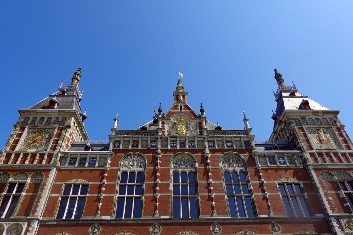 View of the ornate facade of Amsterdam Centraal Station under a clear blue sky.
