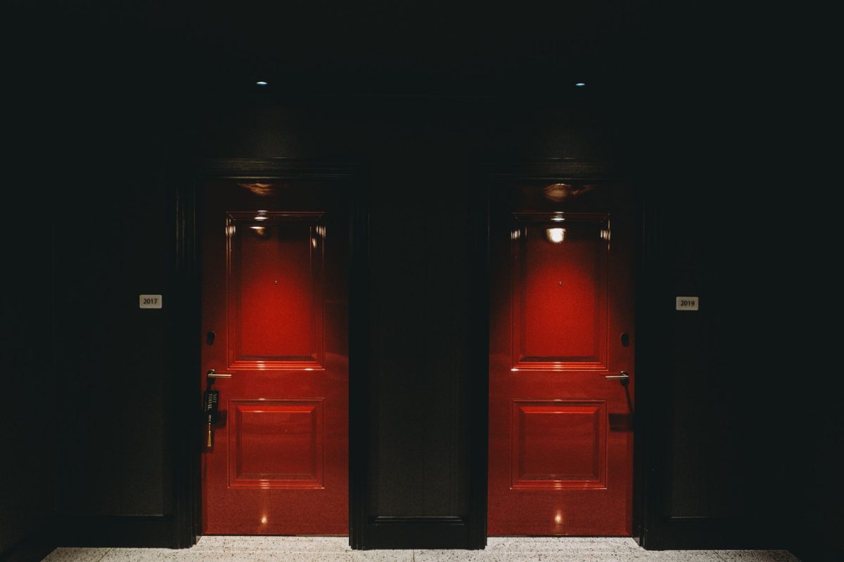5 Hotel Booking Details Families Often Wish They Checked Before Arrival 1 Moody image of two illuminated red doors in a dark hotel hallway, creating a mysterious ambiance.