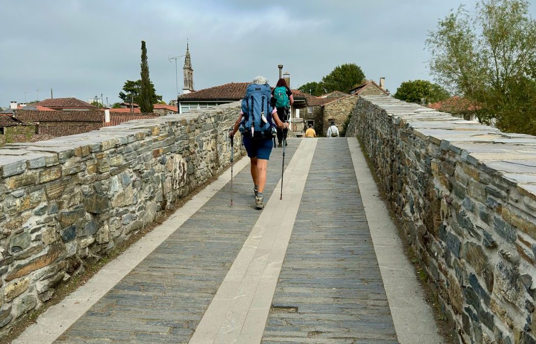 Two hikers with backpacks walking on an ancient stone pathway under a cloudy sky.