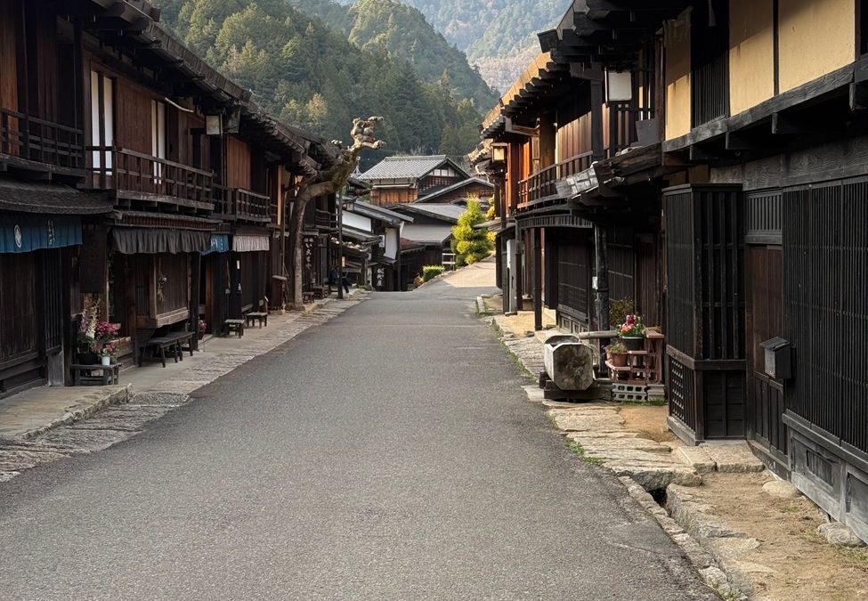 Explore a peaceful Japanese village street with traditional wooden houses and mountain views.