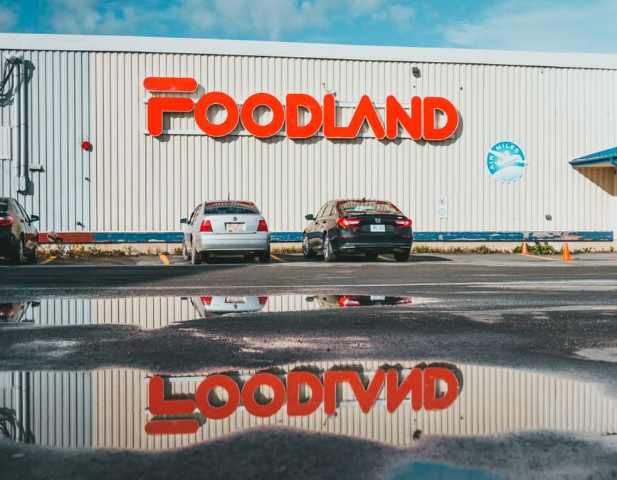 Exterior view of Foodland supermarket with reflection on wet road and parked cars.