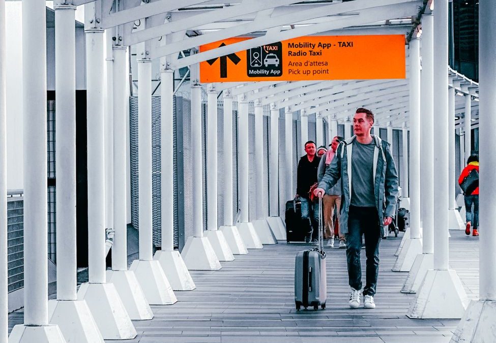 Travelers walking through a modern airport walkway with luggage, heading towards a taxi pickup point.