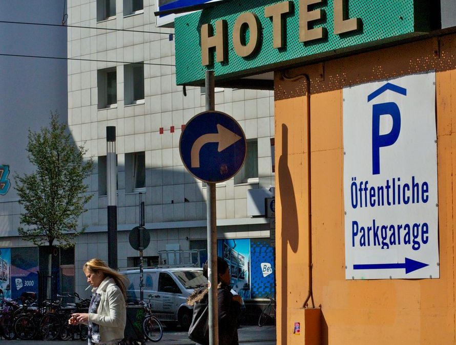 Street view featuring hotel and parking signs with pedestrians in an urban setting.