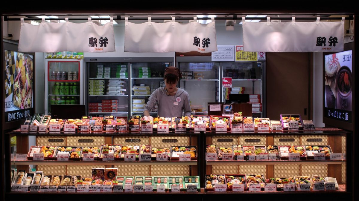 A woman arranges bento boxes in a bustling Tokyo shop, showcasing authentic Japanese culture.
