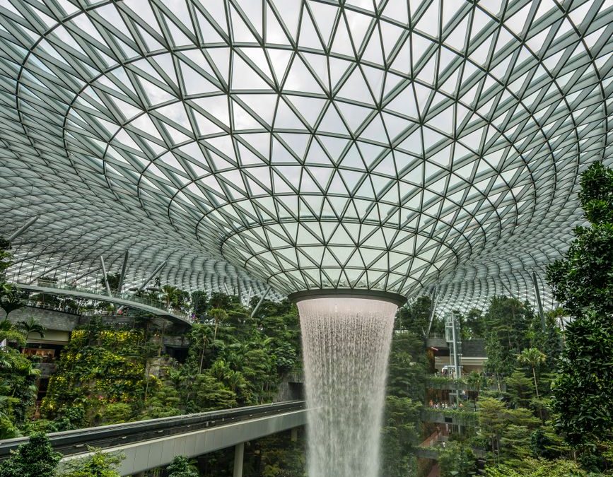 Stunning indoor waterfall surrounded by lush greenery and modern architecture at Singapore&amp;amp;#39;s Jewel Changi Airport.