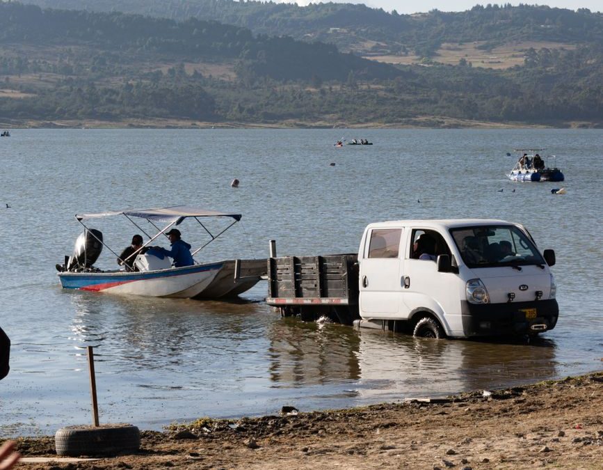 A truck towing a motorboat from a scenic lakeshore under a clear sky.