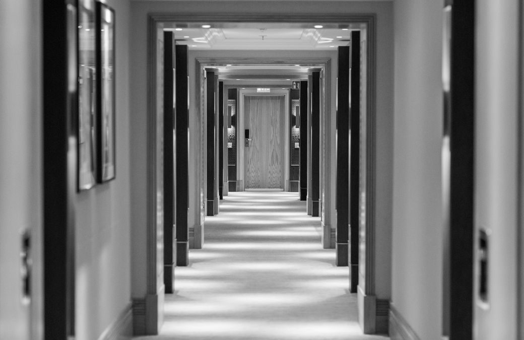 A symmetrical black and white view of a hotel corridor with illuminated lighting and doorways.
