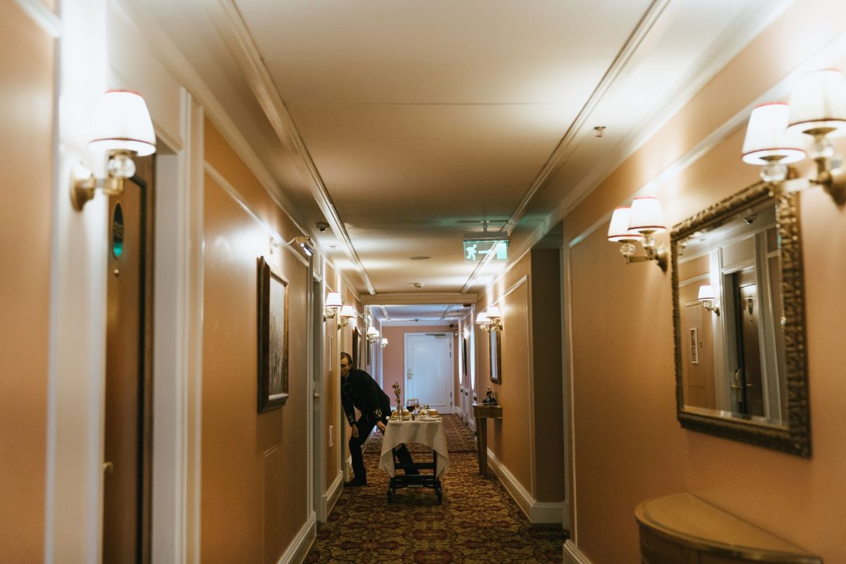 5 Hotel Habits That Make Travelers Seem Unprepared 3 A hotel hallway with a staff member and room service trolley near guest rooms.