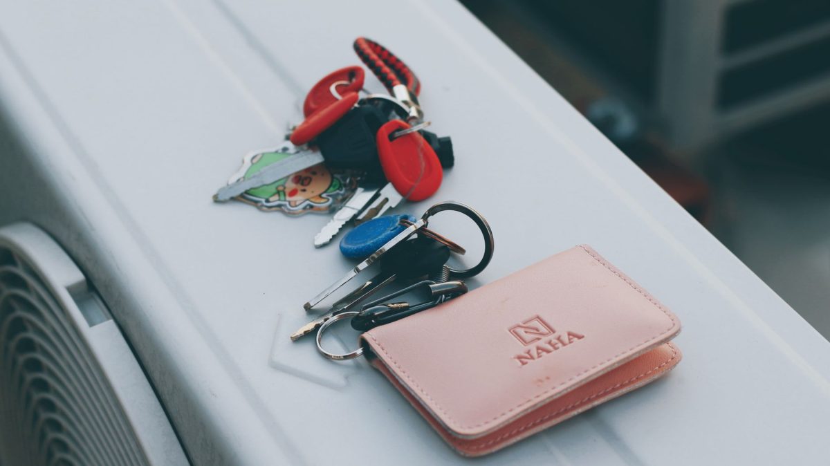 A set of keys with a cute keychain next to an elegant leather wallet on a white surface.