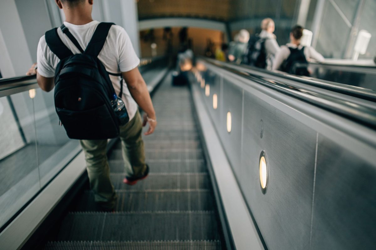 Passengers with backpacks riding an escalator indoors, capturing a travel and commute theme.