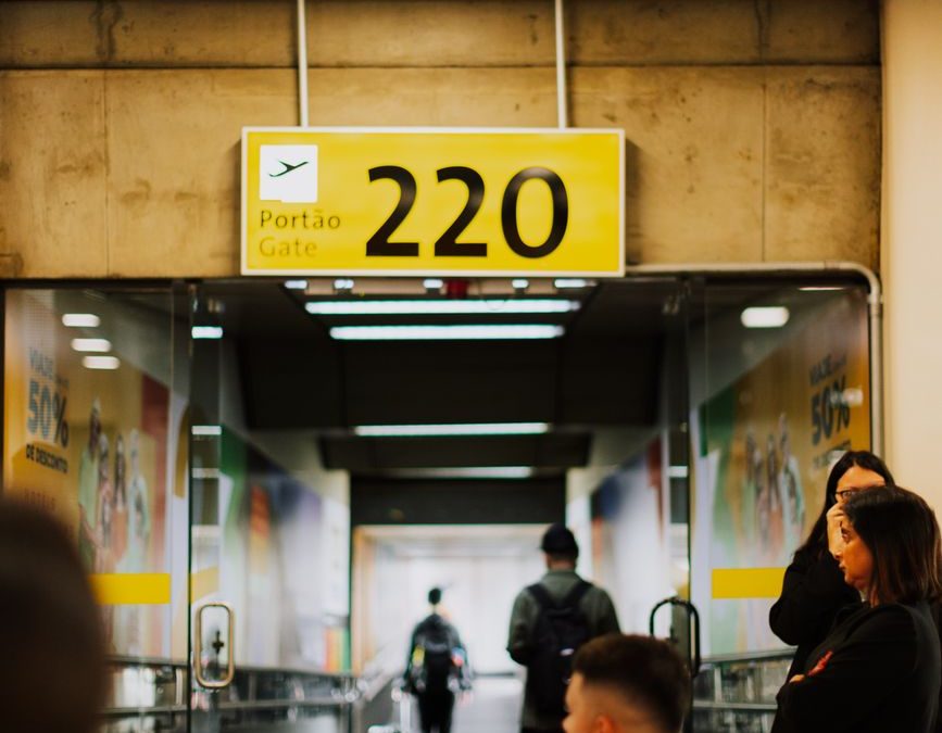 Travelers waiting at a bustling airport gate with a focus on the entrance and sign.