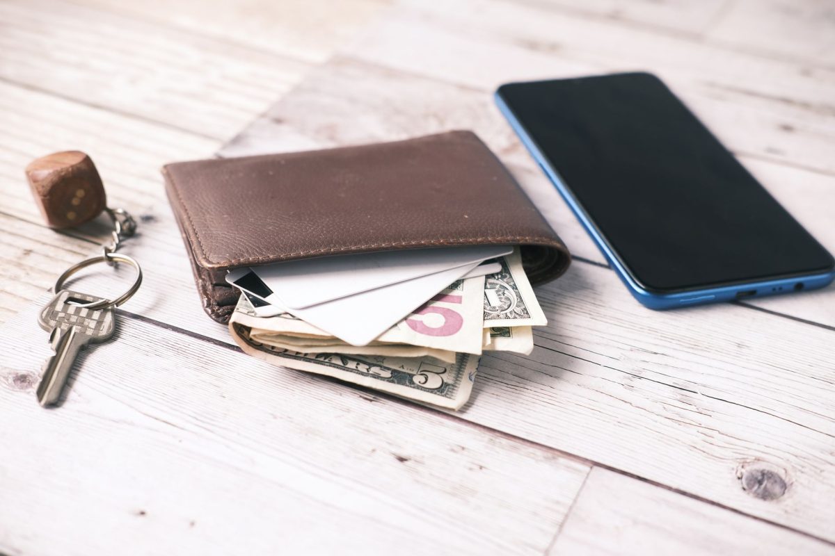 Close up of a wallet with cash, smartphone, and keys on a wooden surface.