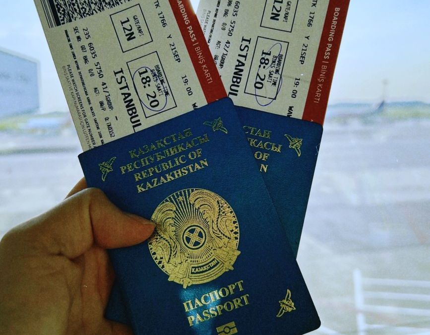 A Kazakhstan passport holds two airline tickets against an airport backdrop in Warsaw, Poland.